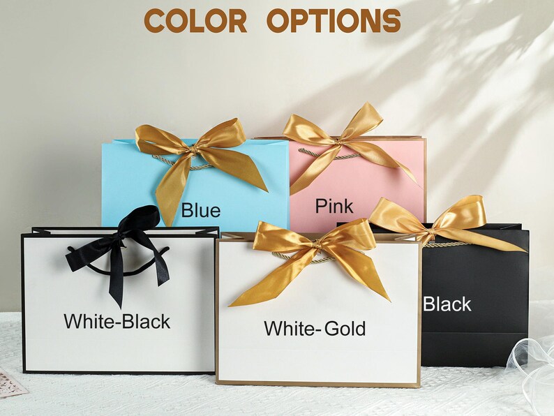 May include: Five gift bags with different colored ribbons and labels. The bags are white, blue, pink, black, and white with gold ribbon. The labels read "White-Black", "Blue", "Pink", "Black", and "White-Gold".