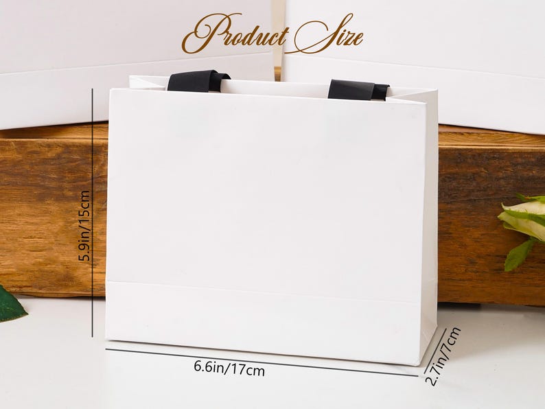 K&ouml;nnte beinhalten: Eine wei&szlig;e Geschenkt&uuml;te aus Papier mit schwarzen Bandhenkeln. Die T&uuml;te tr&auml;gt die Aufschrift Product Size und enth&auml;lt Ma&szlig;linien, die eine H&ouml;he von 15 cm, eine Breite von 17 cm und eine Tiefe von 7 cm f&uuml;r den rechteckigen Boden angeben.