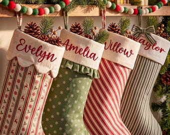 Peut inclure: Quatre chaussettes de Noël personnalisées suspendues en rangée. Chaque chaussette présente un revers blanc avec un prénom brodé en écriture rouge : Evelyn, Amelia, Willow et Taylor. Les motifs incluent des rennes rouges, des flocons blancs, des rayures rouges et vertes.