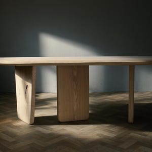 May include: A light wood oval table with three legs. The table has a natural wood finish and is made of solid wood. The table is sitting on a wooden floor.