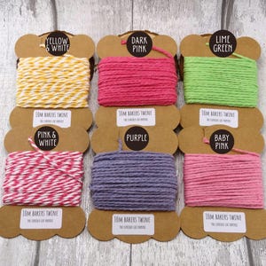 May include: Six spools of baker's twine in various colours, including yellow and white, dark pink, lime green, pink and white, purple, and baby pink. Each spool is labelled with the colour and "10M Bakers Twine The Curious Cat Paperie."