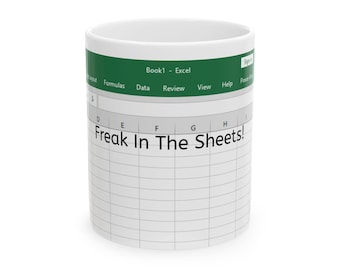 Puede incluir: Taza de cerámica blanca con una banda verde que presenta elementos de la interfaz del software Excel. La taza muestra el texto "Freak In The Sheets!" en negrita negra, sobre un fondo de cuadrícula, evocando una hoja de cálculo.