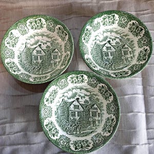 Op de afbeelding: Drie groen-witte keramische kommen met een gedetailleerde landschapsscène. De kommen hebben een decoratieve bloemenrand en een centraal beeld van een gebouw met mensen en paarden. De kommen zijn geplaatst op een lichtgrijze ondergrond.