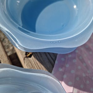 Peut inclure: Deux bols en verre bleu clair avec un bord ondulé et festonné. Le bol supérieur présente le texte en relief 56. 4 sur son bord intérieur. Le verre a une finition lisse et translucide avec des variations subtiles de couleur dans la structure.