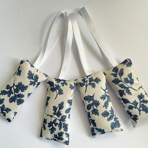May include: Four beige fabric sachets with a blue leaf pattern and white ribbon ties.
