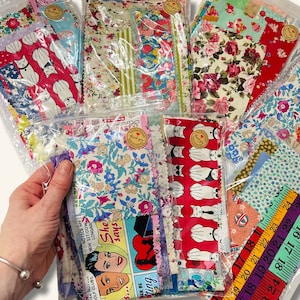 May include: A collection of fabric scraps in various patterns and colours, including floral, geometric, and cartoon designs. The scraps are organised in clear plastic bags and labelled with "thank you" tags.