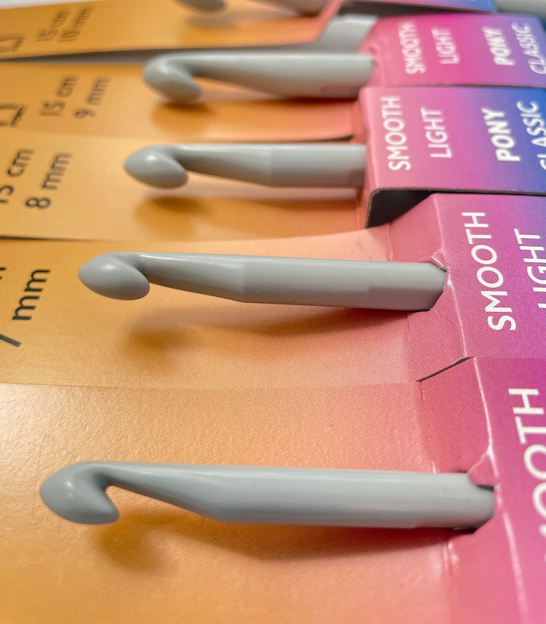 May include: A set of gray crochet hooks with different sizes labeled in millimeters. The hooks are arranged in a row on a colorful background with the words "Smooth", "Light", "Pony", and "Classic" printed on the labels.