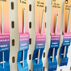 May include: Five white crochet hooks with different sizes, labeled with their size in millimeters and centimeters. The hooks are labeled "Smooth Durable" and "Pony Classic".