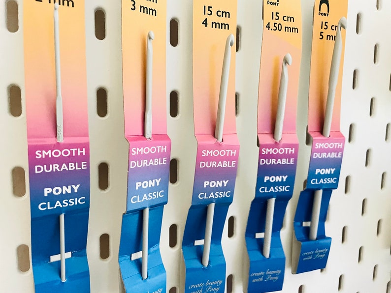 May include: Five white crochet hooks with different sizes, labeled with their size in millimeters and centimeters. The hooks are labeled "Smooth Durable" and "Pony Classic".