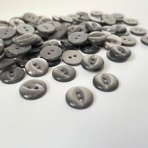May include: A pile of gray plastic buttons with two holes each. The buttons have a slightly iridescent finish.