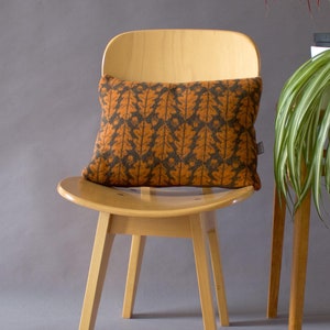 May include: A brown and orange patterned cushion sits on a light wood chair with a curved back. The chair has four legs and is sitting on a grey surface.