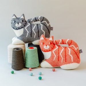 May include: Two knitted cat-shaped plush toys, one gray and white, the other orange and white, with yarn spools in the background.