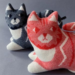 May include: Two knitted cat-shaped plush toys. One is gray and white with black stripes, the other is white with red stripes. Both have black eyes and a white nose.