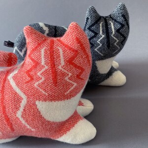 May include: Two knitted cat toys, one red and white and one blue and white. The red and white cat is in the foreground and the blue and white cat is in the background.