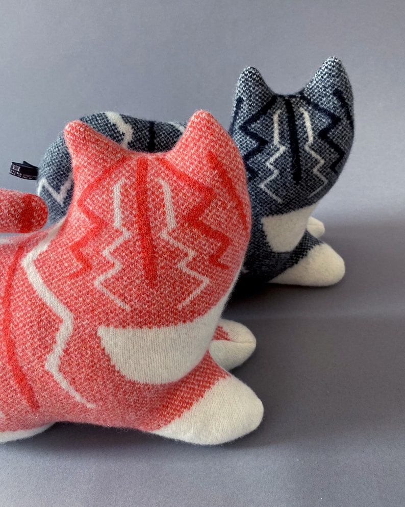 May include: Two knitted cat toys, one red and white and one blue and white. The red and white cat is in the foreground and the blue and white cat is in the background.
