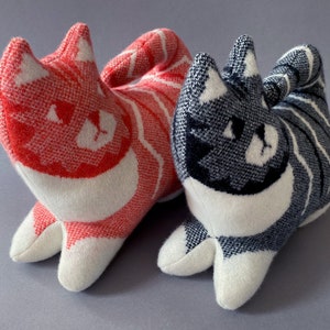 May include: Two plush cat toys, one red and white striped and the other gray and white striped. Both have white faces with black eyes and a black nose.