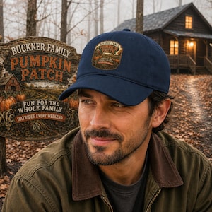 May include: A navy blue baseball cap featuring a rectangular patch on the front. The patch displays an illustration of a pumpkin patch with the text BUCKNER FAMILY PUMPKIN PATCH FUN FOR THE WHOLE FAMILY. The cap has a curved brim and a structured crown.