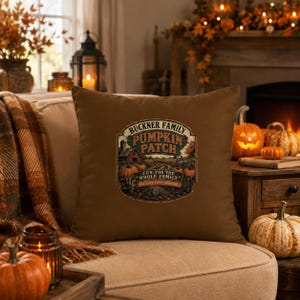 May include: A brown square throw pillow featuring a central graphic with the text BUCKNER FAMILY PUMPKIN PATCH FUN FOR THE WHOLE FAMILY HAYRIDES EVERY WEEKEND. The illustration depicts a farm scene with pumpkins, a barn, and a silo.