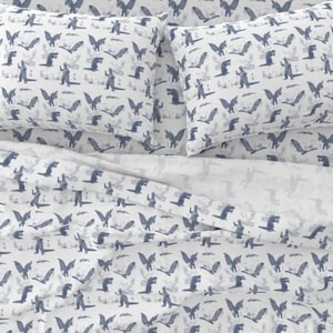 May include: White bedding with a blue and white pattern of a monster with wings. The pattern is repeated all over the bedding.