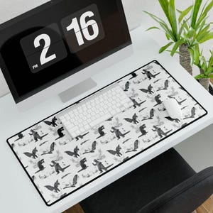 Può includere: Un tappetino da scrivania bianco con un motivo ripetitivo in bianco e nero di una silhouette di mostro. Sulla scrivania ci sono una tastiera, un mouse e un monitor del computer.
