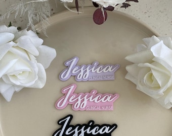 May include: Three name tags with the name "Jessica" and the title "Clinical Nurse" written in cursive. The name tags are in different colors: purple, pink, and black.