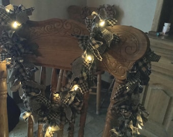 May include: A wooden chair with a decorative back is adorned with a garland of black and white checkered fabric bows. Small, warm white lights are interspersed throughout the garland, creating a cozy, festive atmosphere. The chair is part of a rustic decor.