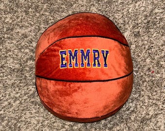 May include: A plush orange basketball with black stitching and the name "EMMRY" embroidered in purple and yellow letters.