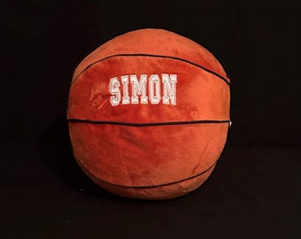 May include: A plush orange basketball with black stitching and the name "SIMON" embroidered in white.