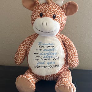 May include: A plush giraffe toy with a brown and orange patterned body and a white face. The giraffe has a blue embroidered message on its chest that reads "Rowan. You are my angel, my darling, my star... my love will find you wherever you are."