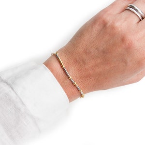 以下が含まれることがあります： シンプルなデザインのシルバーとゴールドのビーズブレスレット。ブレスレットは手首に着用されています。