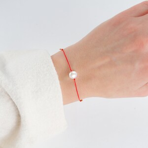 May include: A red string bracelet with a single white pearl charm.