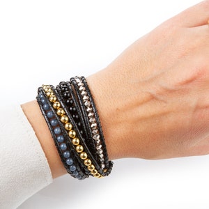 May include: A set of layered bracelets featuring black leather, gold beads, gray beads, and silver beads.
