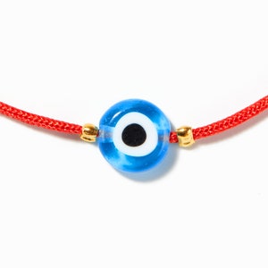 May include: A red string bracelet with a blue evil eye charm. The charm has a white circle with a black pupil in the centre.