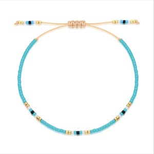 May include: A turquoise blue beaded bracelet with white and black accents. The bracelet is made with small, round beads and has a simple, adjustable closure.