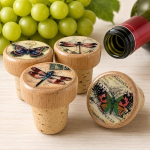 May include: Four wooden bottle stoppers with cork bases. Three stoppers feature colourful butterfly and dragonfly illustrations on their circular tops, while one displays a butterfly with the text MAGASINS PARIS printed on a vintage-style background.