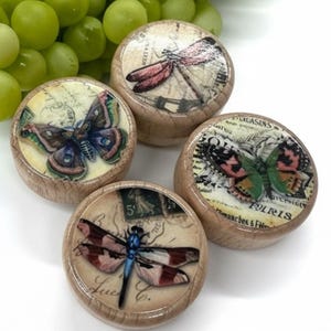 Puede incluir: Cuatro pomos de madera para armarios con diseños de insectos y escritura vintage. Los pomos presentan mariposas y libélulas en tonos rosa, azul y verde. Los pomos son redondos y tienen una veta de madera marrón claro.