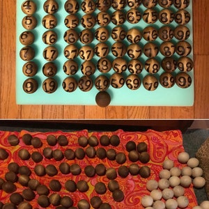 May include: A set of 90 wooden balls with black numbers painted on them. The balls are arranged in a grid on a light blue surface. The balls are used for a game of bingo.