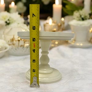 May include: White cake stand with a round top and a pedestal base. The stand is 6 inches tall and measures 7 inches in diameter.