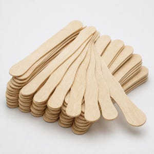 May include: A large stack of light-coloured wooden craft sticks, each featuring a smooth, flat surface with rounded ends. The sticks are arranged in a fan-like pattern, showcasing their natural grain and uniform, elongated shape for various projects.