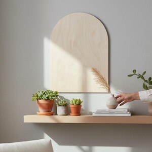 Puede incluir: Una placa de pared de madera clara en forma de arco con un acabado de grano liso. La placa est&aacute; montada sobre un estante horizontal que sostiene tres peque&ntilde;as suculentas en macetas de terracota y grises, junto a un jarr&oacute;n y libros.