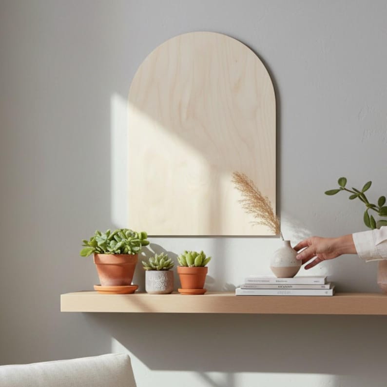 Puede incluir: Una placa de pared de madera clara en forma de arco con un acabado de grano liso. La placa est&aacute; montada sobre un estante horizontal que sostiene tres peque&ntilde;as suculentas en macetas de terracota y grises, junto a un jarr&oacute;n y libros.