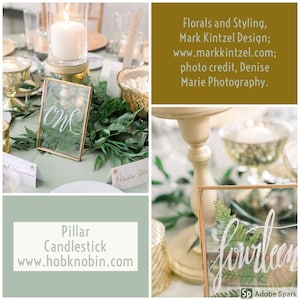 May include: A gold pillar candlestick with a white candle on top. The candlestick is on a table with a green tablecloth. There are two glass frames with the numbers "one" and "fourteen" written in white calligraphy. The table is decorated with greenery and gold accents.
