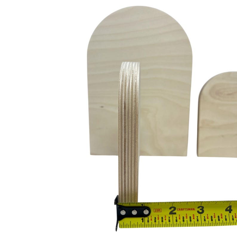 Puede incluir: Dos placas de madera clara sin terminar en forma de arco con veta visible. Una cinta m&eacute;trica amarilla Craftsman est&aacute; colocada en la base de la placa m&aacute;s grande, mostrando un grosor de aproximadamente 1,9 cm para el material de contrachapado.