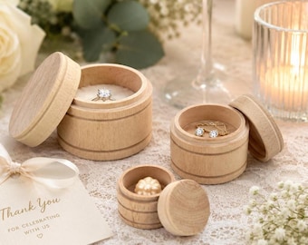 May include: Three round light-colored wooden boxes with removable lids. The largest box contains a silver ring with a clear stone. The medium box holds a pair of small silver stud earrings. The smallest box contains a single cream-colored pearl.