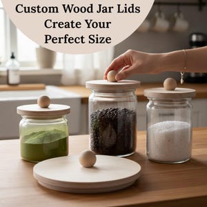 May include: Custom wood jar lids with a round wooden knob on top. The lids are on glass jars filled with green powder, coffee beans, and white granules. The text on the image says, "Custom Wood Jar Lids Create Your Perfect Size."