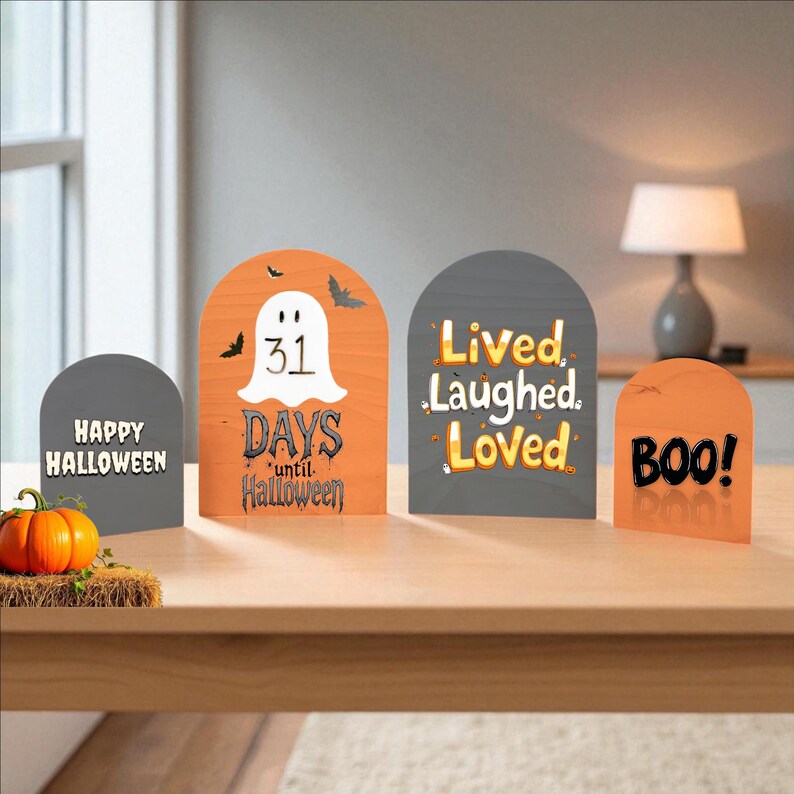 Puede incluir: Cuatro letreros de madera arqueados con temas de Halloween. Un letrero gris dice Happy Halloween, uno naranja muestra un fantasma y 31 Days until Halloween, uno gris dice Lived Laughed Loved y uno naranja dice BOO. Una peque&ntilde;a calabaza est&aacute; cerca.