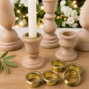 Può includere: Una collezione di candelabri in legno non rifiniti e coppe per candele in ottone. Un portacandele contiene una candela bianca. I portacandele sono di varie dimensioni e forme. Gli articoli sono disposti su una superficie di legno chiaro.