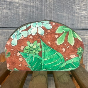 May include: A brown and green fabric pouch with a zipper closure. The pouch features a floral pattern with green leaves and light blue flowers.