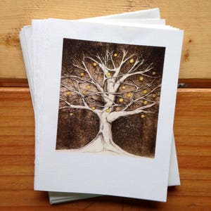 May include: A stack of blank greeting cards with a black and white illustration of a tree with yellow fruit on the front. The tree is set against a dark background.