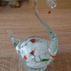 Könnte beinhalten: Eine durchsichtige Glas-Schwan-Figur mit langem, gebogenem Hals und einem kleinen roten Akzent. Der Körper ist mit weißen, orangefarbenen und grünen dekorativen Elementen gefüllt. Die Figur ist ein Dekorationsartikel.